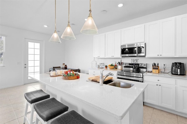 kitchen featuring stainless steel appliances, a center island with sink, decorative light fixtures, and sink