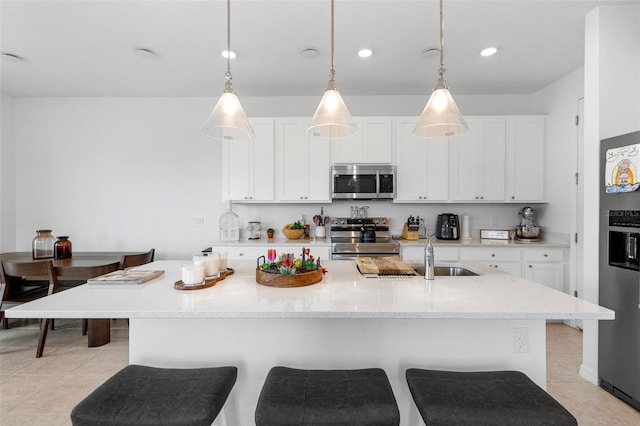 kitchen with hanging light fixtures, an island with sink, white cabinetry, and stainless steel appliances