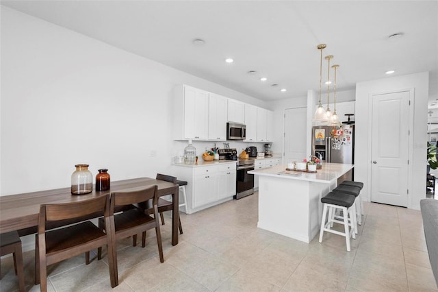 kitchen with a breakfast bar area, white cabinetry, stainless steel appliances, a center island with sink, and decorative light fixtures