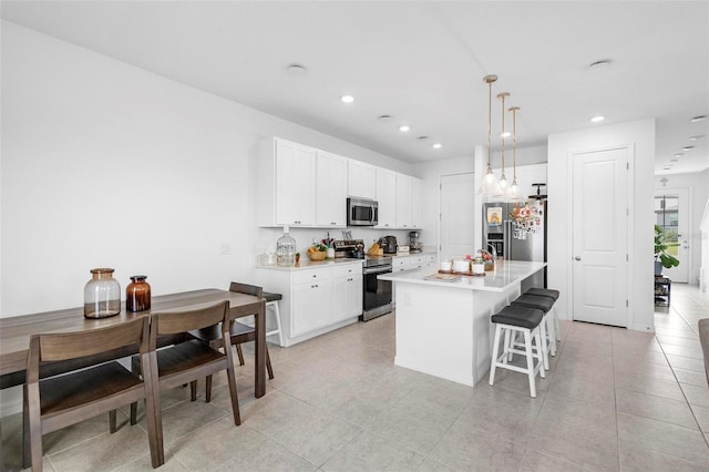 kitchen with white cabinets, an island with sink, stainless steel appliances, and decorative light fixtures