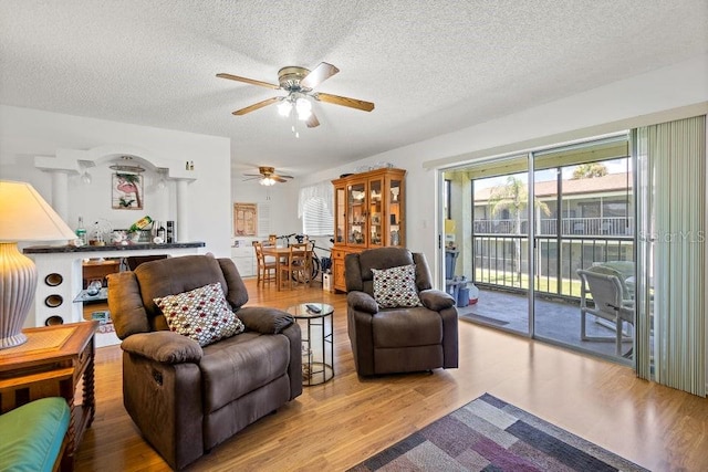 living room featuring a textured ceiling, light wood-type flooring, and ceiling fan