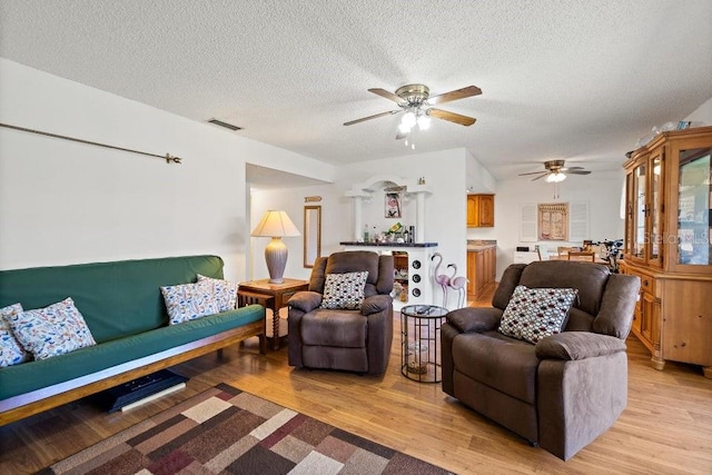 living room with a textured ceiling, light wood-type flooring, and ceiling fan