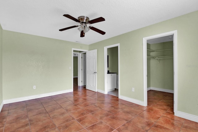 unfurnished bedroom with ceiling fan, a textured ceiling, a closet, a walk in closet, and tile patterned floors