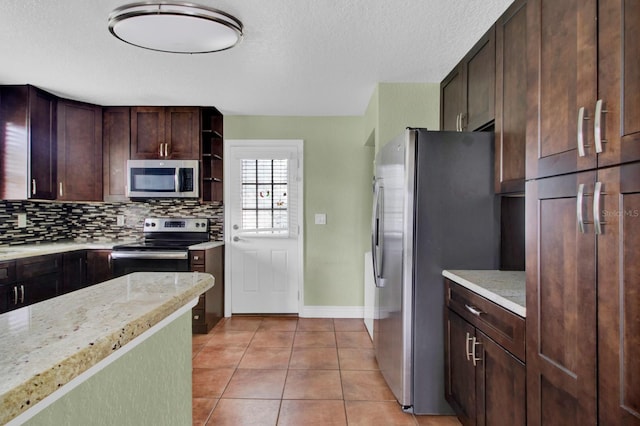 kitchen with tasteful backsplash, dark brown cabinets, light tile patterned floors, appliances with stainless steel finishes, and light stone countertops