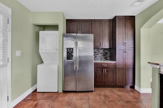 kitchen featuring stainless steel fridge with ice dispenser, tile patterned flooring, tasteful backsplash, and stacked washing maching and dryer