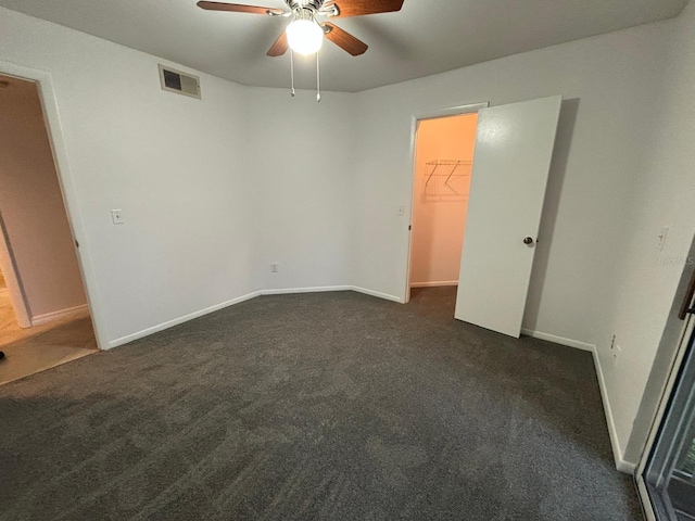 unfurnished bedroom with dark carpet, a spacious closet, and ceiling fan