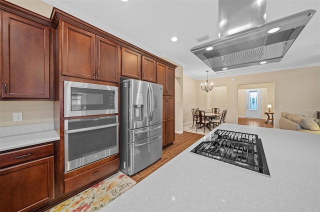 kitchen featuring island exhaust hood, light hardwood / wood-style flooring, an inviting chandelier, appliances with stainless steel finishes, and ornamental molding