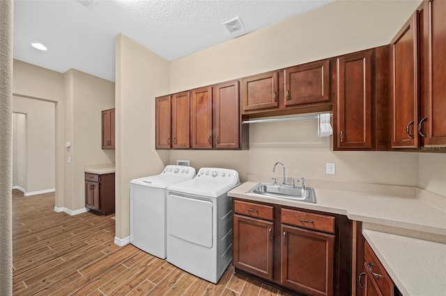 laundry room featuring separate washer and dryer, light wood-type flooring, a textured ceiling, cabinets, and sink