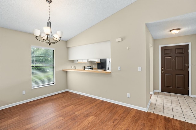 interior space with an inviting chandelier, light wood-type flooring, lofted ceiling, and a textured ceiling