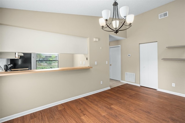 empty room with an inviting chandelier, wood-type flooring, and vaulted ceiling