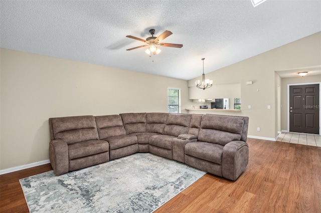 living room featuring ceiling fan with notable chandelier, vaulted ceiling, a textured ceiling, and hardwood / wood-style floors