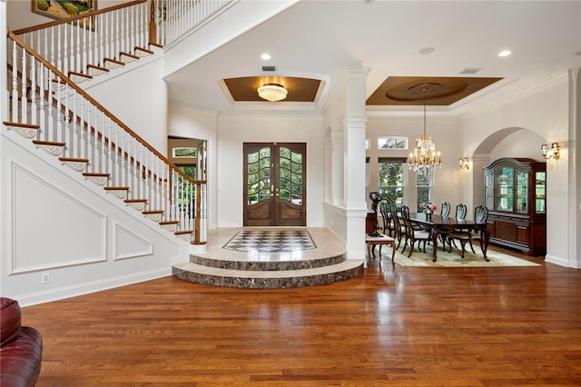 foyer entrance with wood-type flooring, an inviting chandelier, crown molding, a high ceiling, and french doors