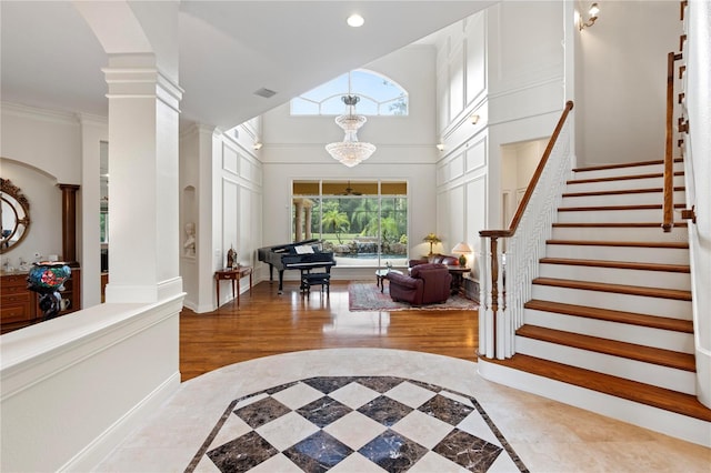 entryway featuring crown molding, a high ceiling, decorative columns, hardwood / wood-style floors, and a chandelier