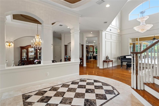 entrance foyer with a towering ceiling, ceiling fan with notable chandelier, ornate columns, crown molding, and hardwood / wood-style floors