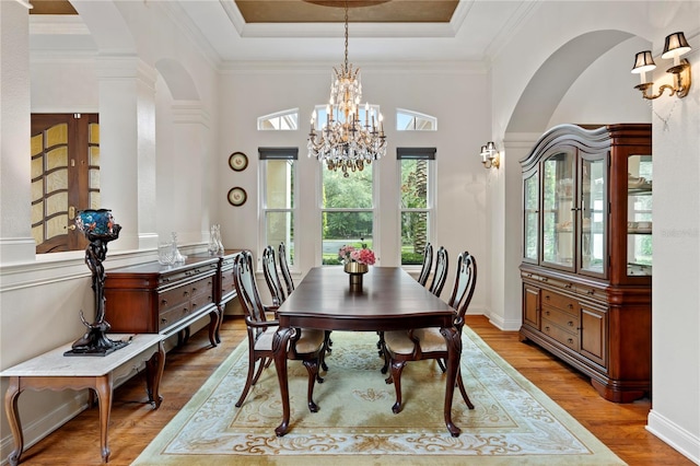 dining space with wood-type flooring, a chandelier, a raised ceiling, and crown molding