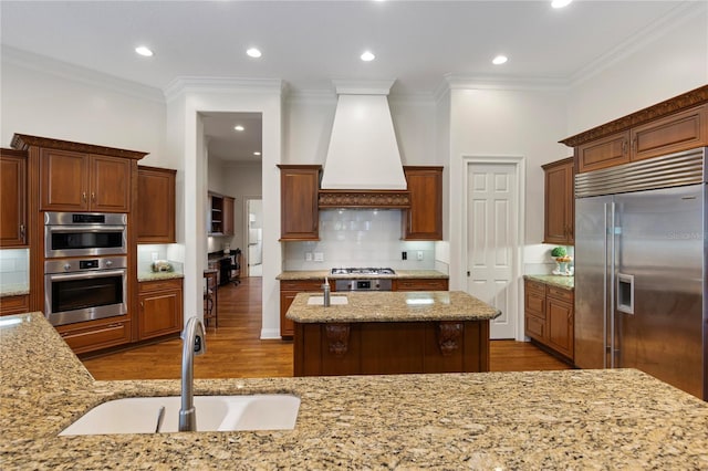 kitchen with appliances with stainless steel finishes, dark hardwood / wood-style flooring, custom exhaust hood, a center island with sink, and sink