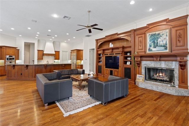 living room with ceiling fan, sink, a high end fireplace, light wood-type flooring, and crown molding