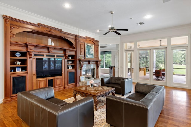 living room featuring light hardwood / wood-style flooring, ceiling fan, a premium fireplace, and ornamental molding