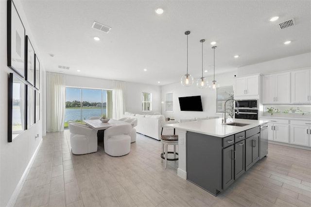 kitchen with sink, hanging light fixtures, an island with sink, light hardwood / wood-style floors, and white cabinetry