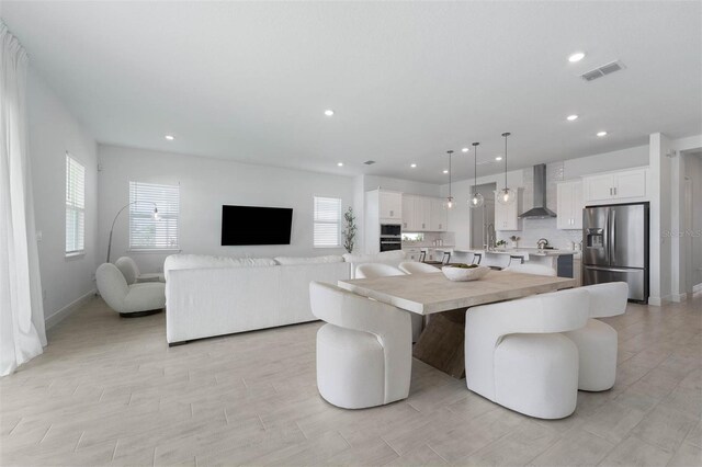 kitchen with wall chimney exhaust hood, stainless steel appliances, pendant lighting, white cabinets, and a kitchen island