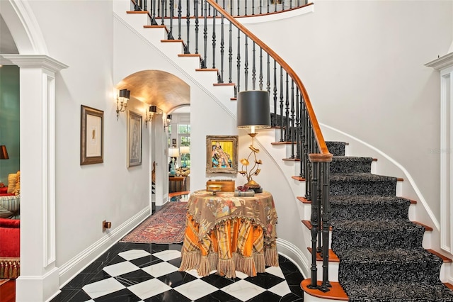 staircase featuring crown molding, a towering ceiling, and ornate columns