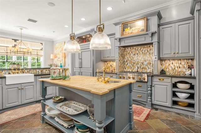 kitchen featuring sink, an island with sink, gray cabinetry, backsplash, and ornamental molding