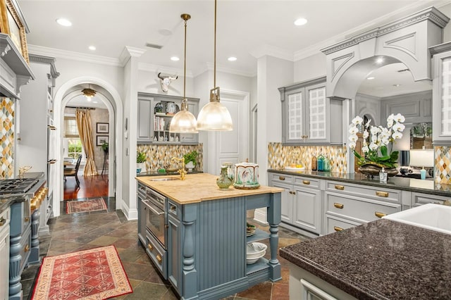 kitchen with a center island, wood counters, tasteful backsplash, hanging light fixtures, and ornamental molding