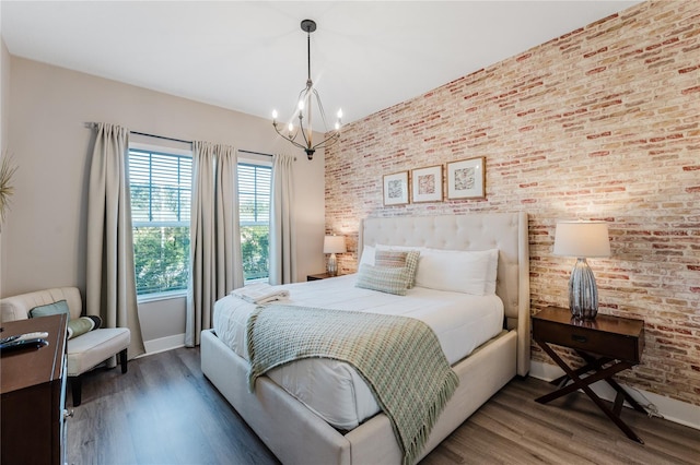 bedroom with dark wood-type flooring, a notable chandelier, and brick wall