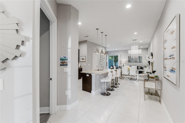 kitchen featuring light stone countertops, light tile patterned flooring, decorative light fixtures, a breakfast bar, and a center island with sink