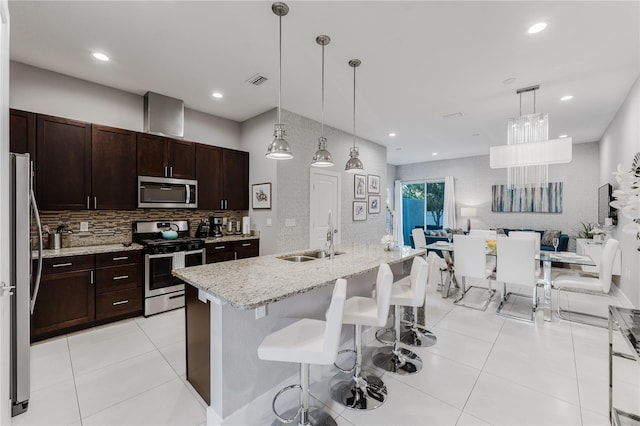 kitchen featuring an island with sink, hanging light fixtures, sink, light stone countertops, and appliances with stainless steel finishes