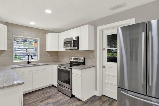 kitchen with sink, tasteful backsplash, appliances with stainless steel finishes, light stone countertops, and white cabinets