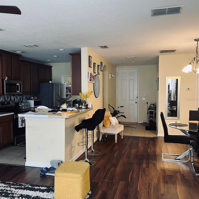 kitchen with black range with electric stovetop, kitchen peninsula, dark wood-type flooring, a kitchen breakfast bar, and refrigerator