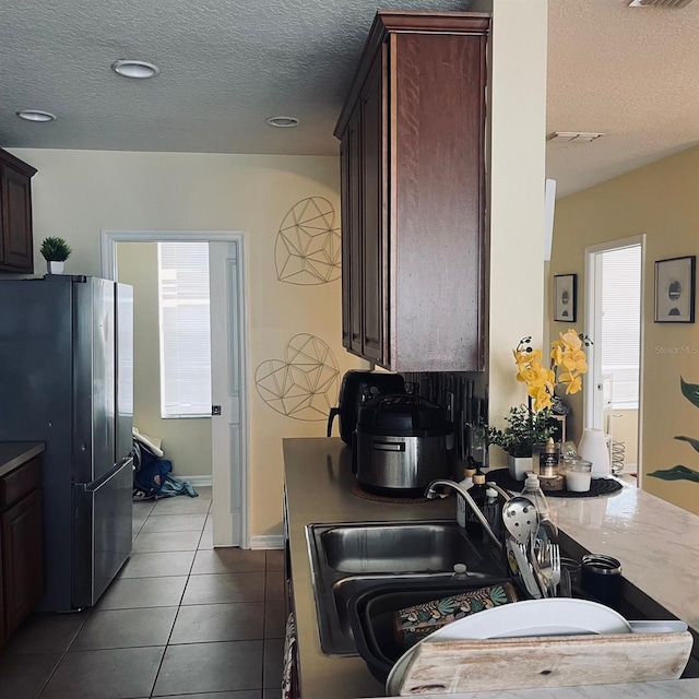 kitchen with dark brown cabinets, a textured ceiling, light tile patterned floors, and stainless steel fridge