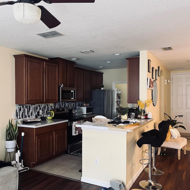 kitchen featuring appliances with stainless steel finishes, tasteful backsplash, kitchen peninsula, a kitchen bar, and light hardwood / wood-style flooring