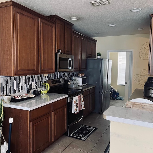 kitchen with appliances with stainless steel finishes, a textured ceiling, light tile patterned floors, and tasteful backsplash