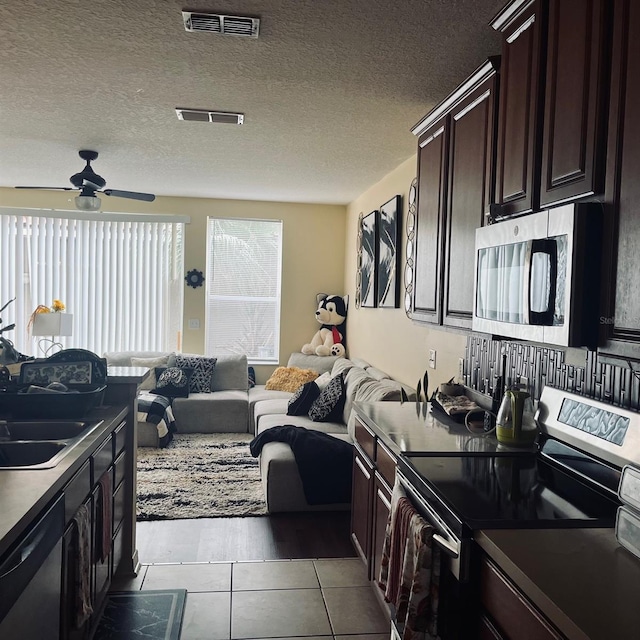 kitchen with dark brown cabinets, a textured ceiling, sink, appliances with stainless steel finishes, and light tile patterned floors