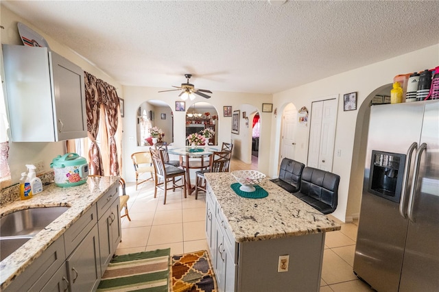 kitchen with stainless steel refrigerator with ice dispenser, gray cabinetry, a center island, light tile patterned floors, and ceiling fan