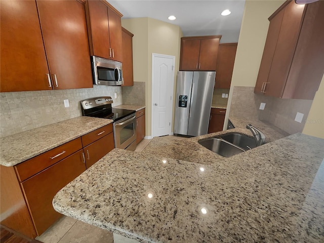 kitchen featuring light stone counters, kitchen peninsula, appliances with stainless steel finishes, and sink