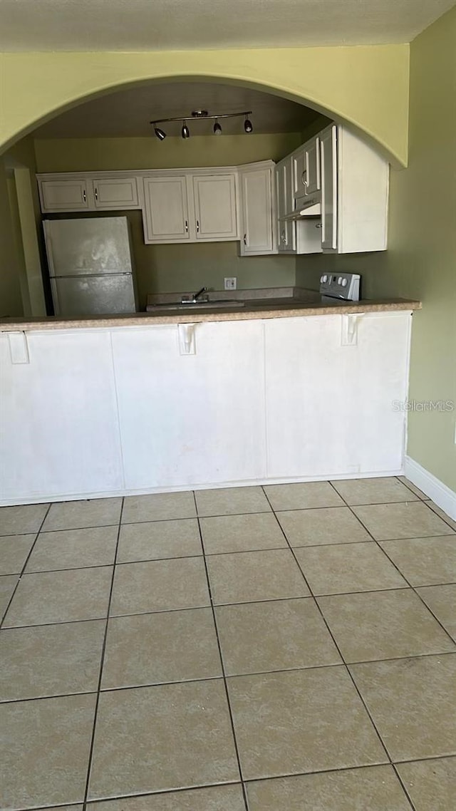 7622 Forest City Rd Unit E, Orlando, FL 32810 - kitchen featuring freestanding refrigerator, white cabinets, light tile patterned flooring, baseboards, and under cabinet range hood