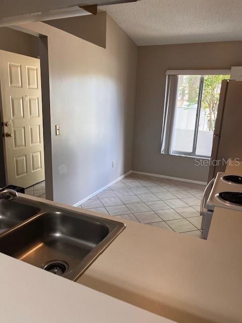 kitchen featuring range with electric stovetop, light tile patterned floors, white fridge, a textured ceiling, and sink