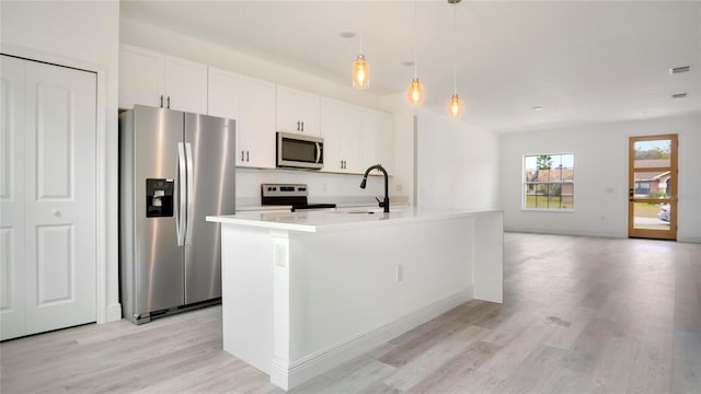 kitchen featuring light hardwood / wood-style floors, a kitchen island with sink, white cabinets, hanging light fixtures, and appliances with stainless steel finishes