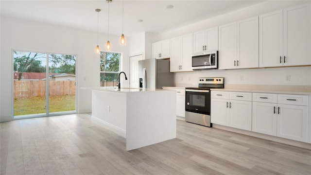 kitchen with pendant lighting, white cabinetry, light hardwood / wood-style flooring, a center island with sink, and appliances with stainless steel finishes