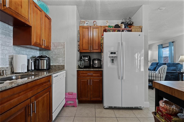 kitchen featuring light tile patterned flooring, tasteful backsplash, dark stone countertops, white appliances, and a textured ceiling