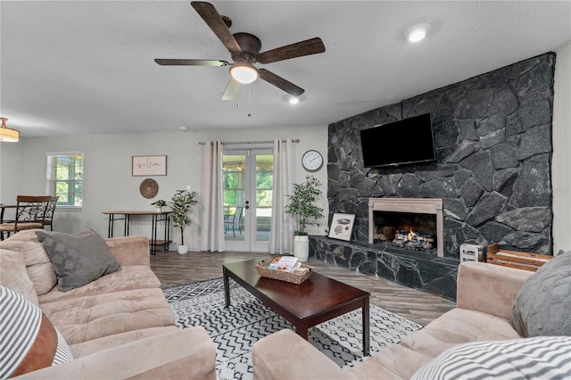 living room featuring hardwood / wood-style flooring, a stone fireplace, ceiling fan, and a wealth of natural light