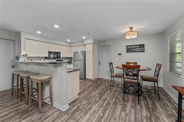 kitchen with stainless steel fridge, kitchen peninsula, white cabinetry, dark hardwood / wood-style floors, and a breakfast bar area