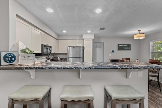 kitchen featuring a breakfast bar area, stainless steel fridge, kitchen peninsula, and white cabinetry