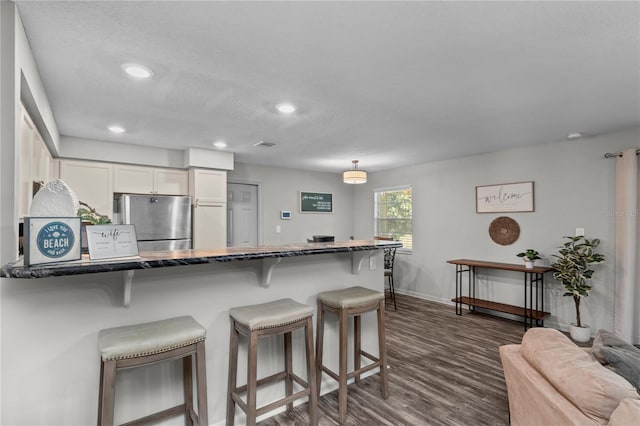 kitchen with stainless steel fridge, white cabinetry, dark hardwood / wood-style flooring, a textured ceiling, and a kitchen bar