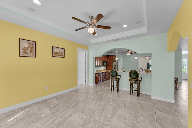 living room featuring a raised ceiling, ceiling fan, and crown molding