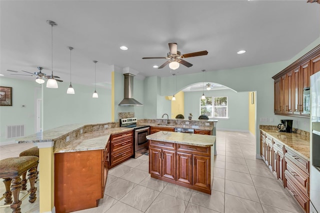 kitchen featuring pendant lighting, wall chimney range hood, sink, appliances with stainless steel finishes, and kitchen peninsula