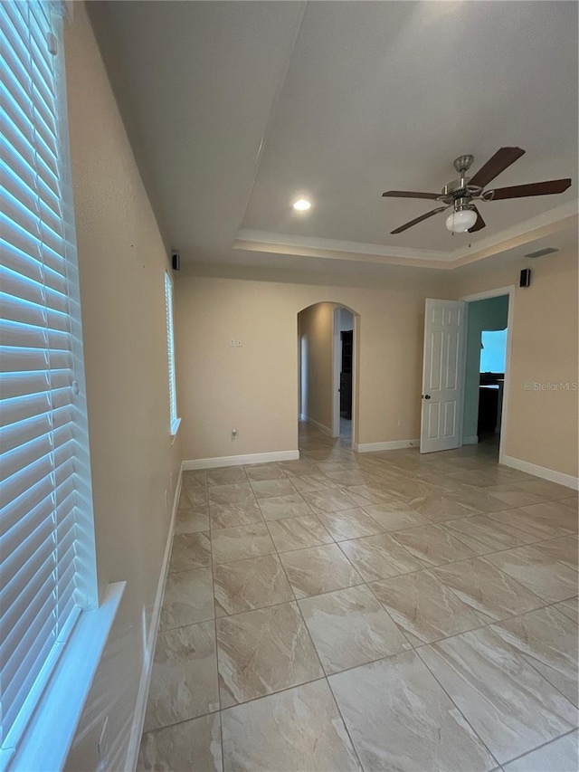 spare room with a tray ceiling, a wealth of natural light, and ceiling fan